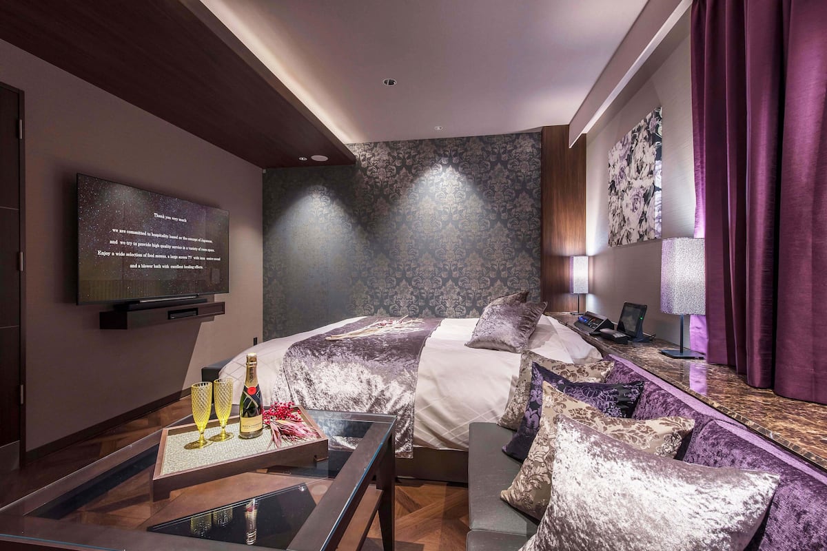 Een moderne hotelkamer met een groot bed, een bank, een televisie en een glazen salontafel met een fles en glazen erop.