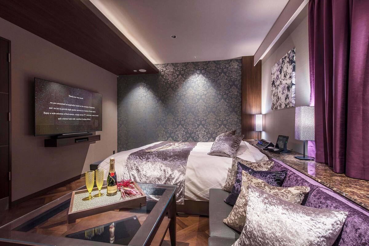 Een moderne hotelkamer met een bed, een bank, een televisie en een tafel met glazen en een fles.