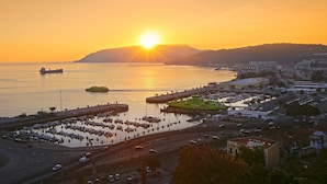 A coastal cityscape at sunset with a marina, roads, and buildings.