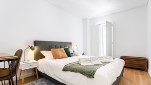 A modern bedroom with a large bed, bedside tables, a desk, and a chair.