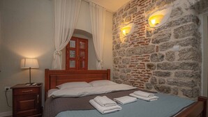 A bedroom with a wooden bed, a nightstand, a stone wall, and a window with curtains.