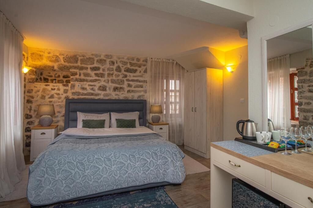 A bedroom with a stone wall, a bed with a patterned bedspread, bedside lamps, a wooden dresser, and a mirror.
