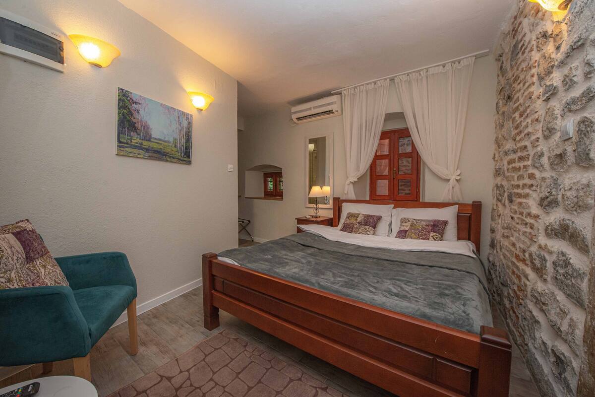 Quarto com cama de madeira, poltrona verde, quadro na parede e parede de pedra.
