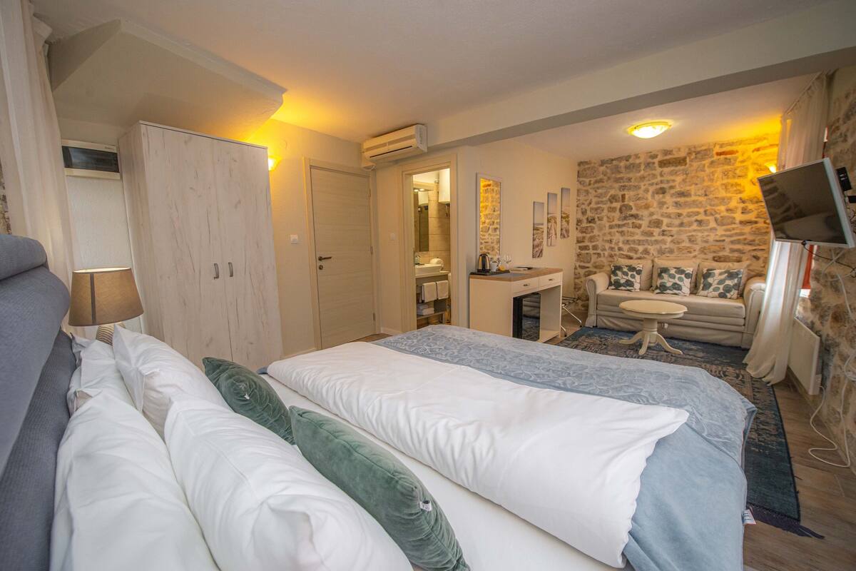 Quarto com cama, guarda-roupa, escrivaninha, sofá e parede de pedra.