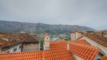 A view of terracotta-tiled rooftops, stone buildings, and a mountainous backdrop.