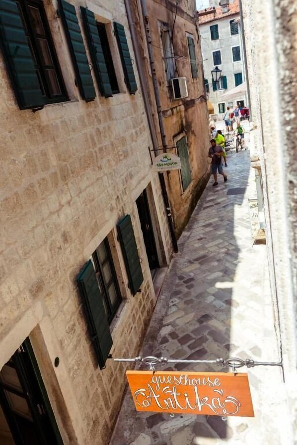 Una calle estrecha con edificios de piedra, un letrero que dice 'guesthouse Antika' y algunas personas caminando.