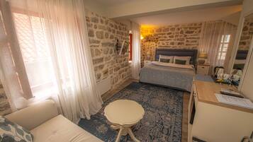 A bedroom with a stone wall, a bed, a small table, a sofa, and a desk with a chair.