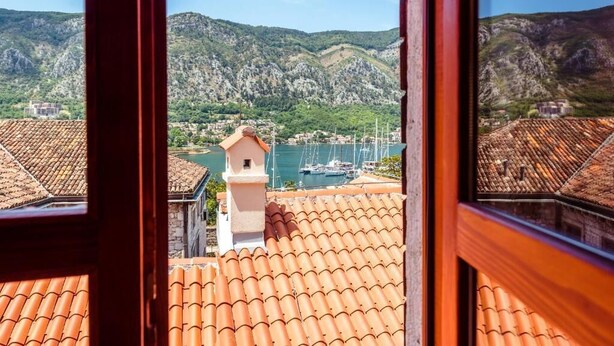 A coastal town with terracotta roofs, a marina, and mountains in the background.