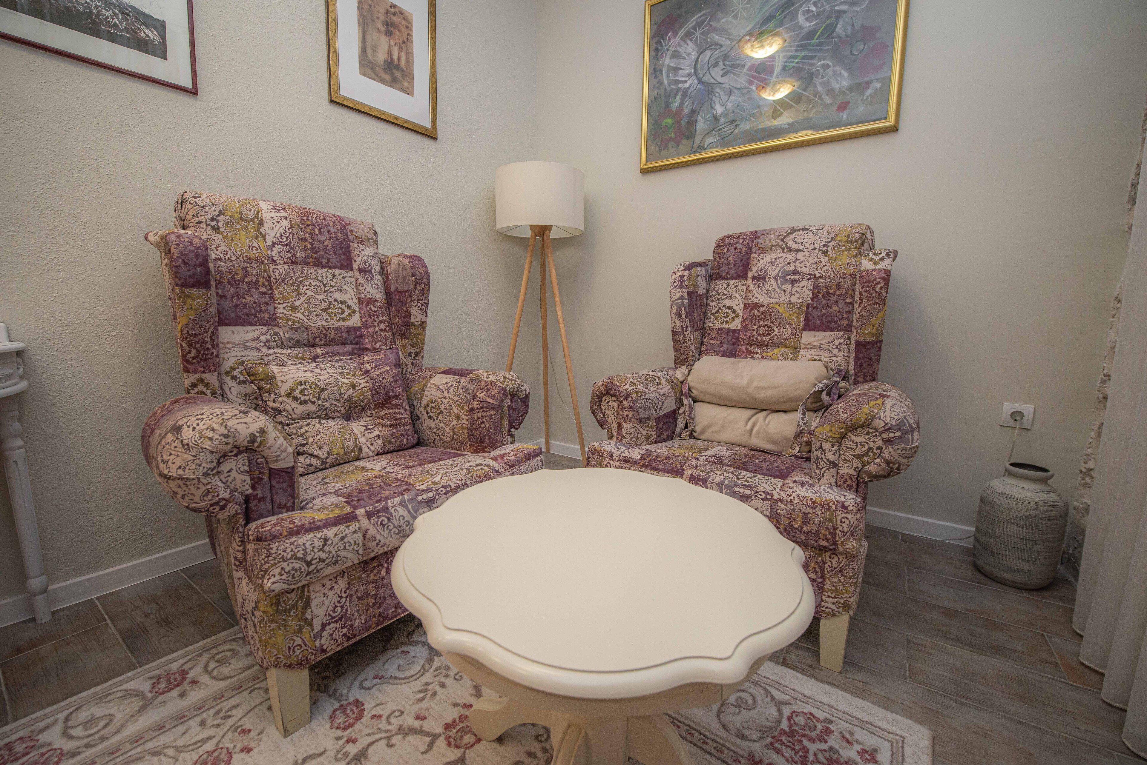 Une pièce comprenant deux fauteuils à motifs, une petite table ronde, un lampadaire et un grand tableau abstrait accroché au mur.