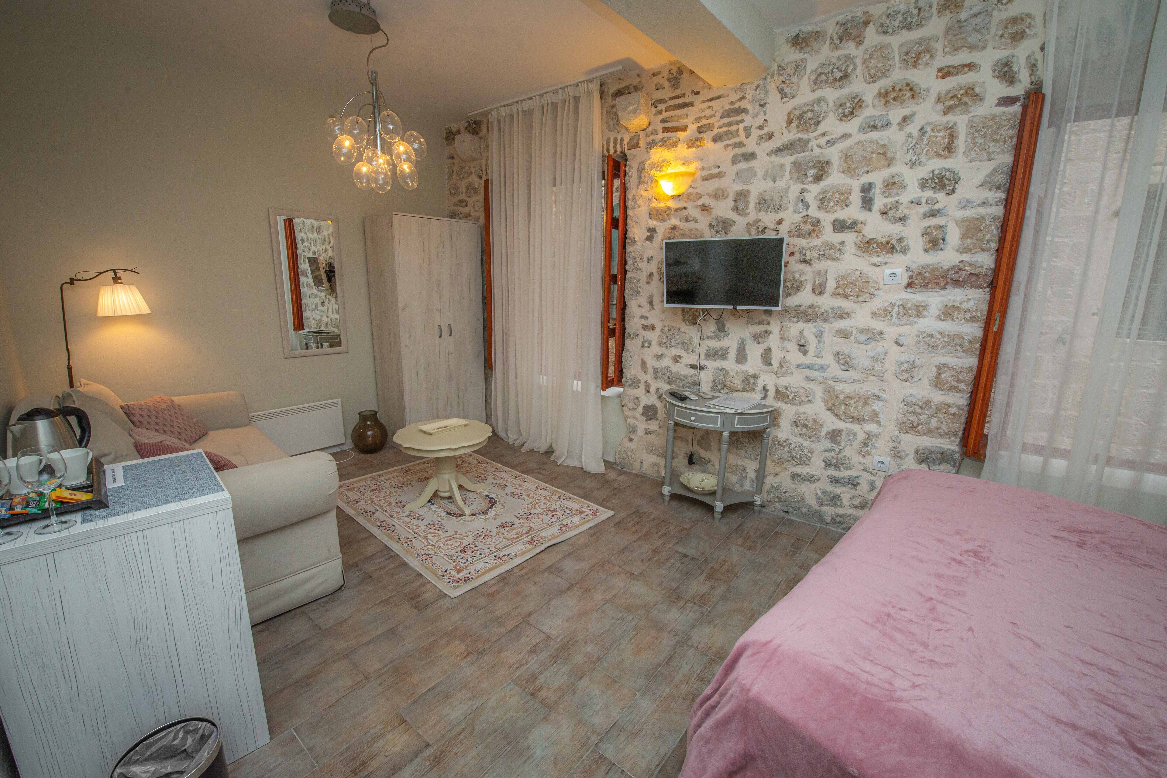 Un dormitorio con pared de piedra, televisor montado, cama, escritorio con lámpara y una mesita pequeña.