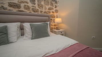 Un dormitorio con pared de piedra, cama con almohadas blancas y verdes, manta rosa y lámpara de noche.