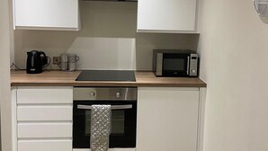 A compact kitchen with white cabinets, a microwave, a kettle, and a toaster on the countertop. - Captivating 2-bed Apartment in Bradford (Bradford)
