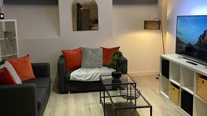 A modern living room with a black sofa, a glass coffee table, and a TV on a white stand. - Captivating 2-bed Apartment in Bradford (Bradford)