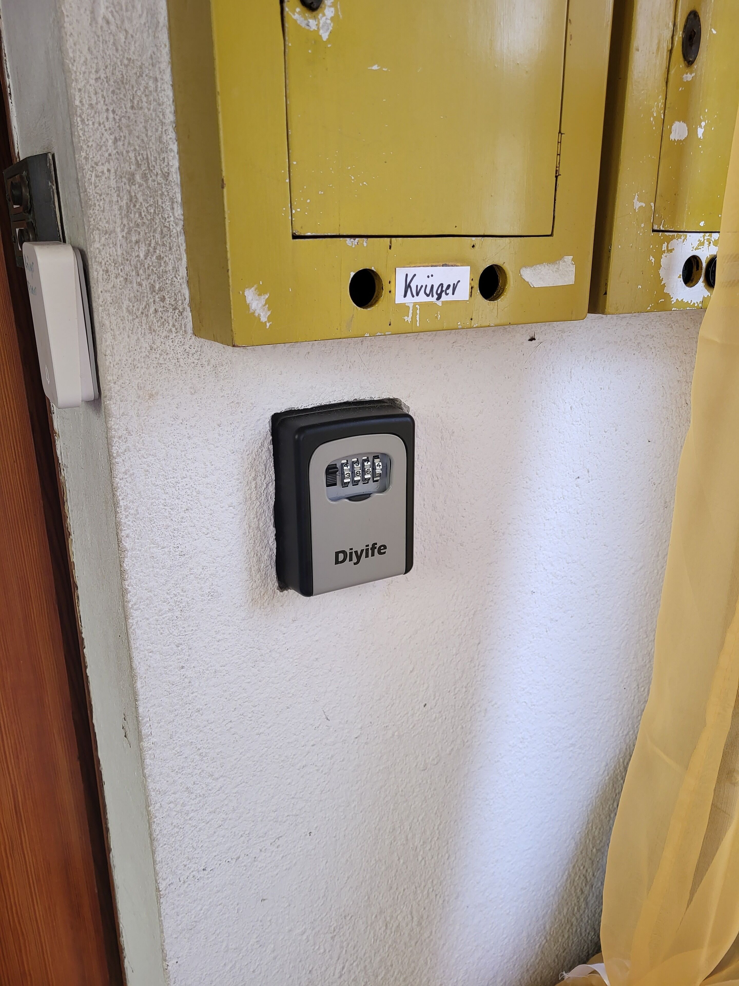 Un clavier de sécurité portant l’inscription « Diyife » et un panneau jaune avec le mot « Krüger » sur un mur blanc.