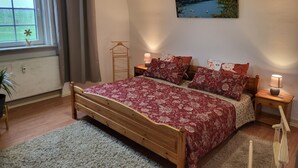 A bedroom with a wooden bed, floral bedding, a view of a lake through a window, and a painting of a landscape on the wall.
