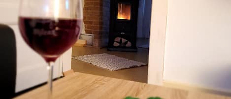 A room with a fireplace, a glass of red wine, and a table with flowers.