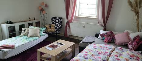 A well-lit room with two beds, a sofa, a small table, and a cabinet.