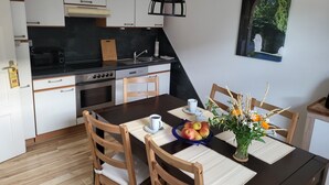A modern kitchen with white cabinets, a black countertop, and a dining area with wooden chairs and a table set with a vase of flowers and a bowl of fruit.