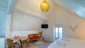 Ein moderner, gut beleuchteter Raum mit einem Bett, einer Couch, einem Esstisch und einem an der Wand befestigten Fernseher.