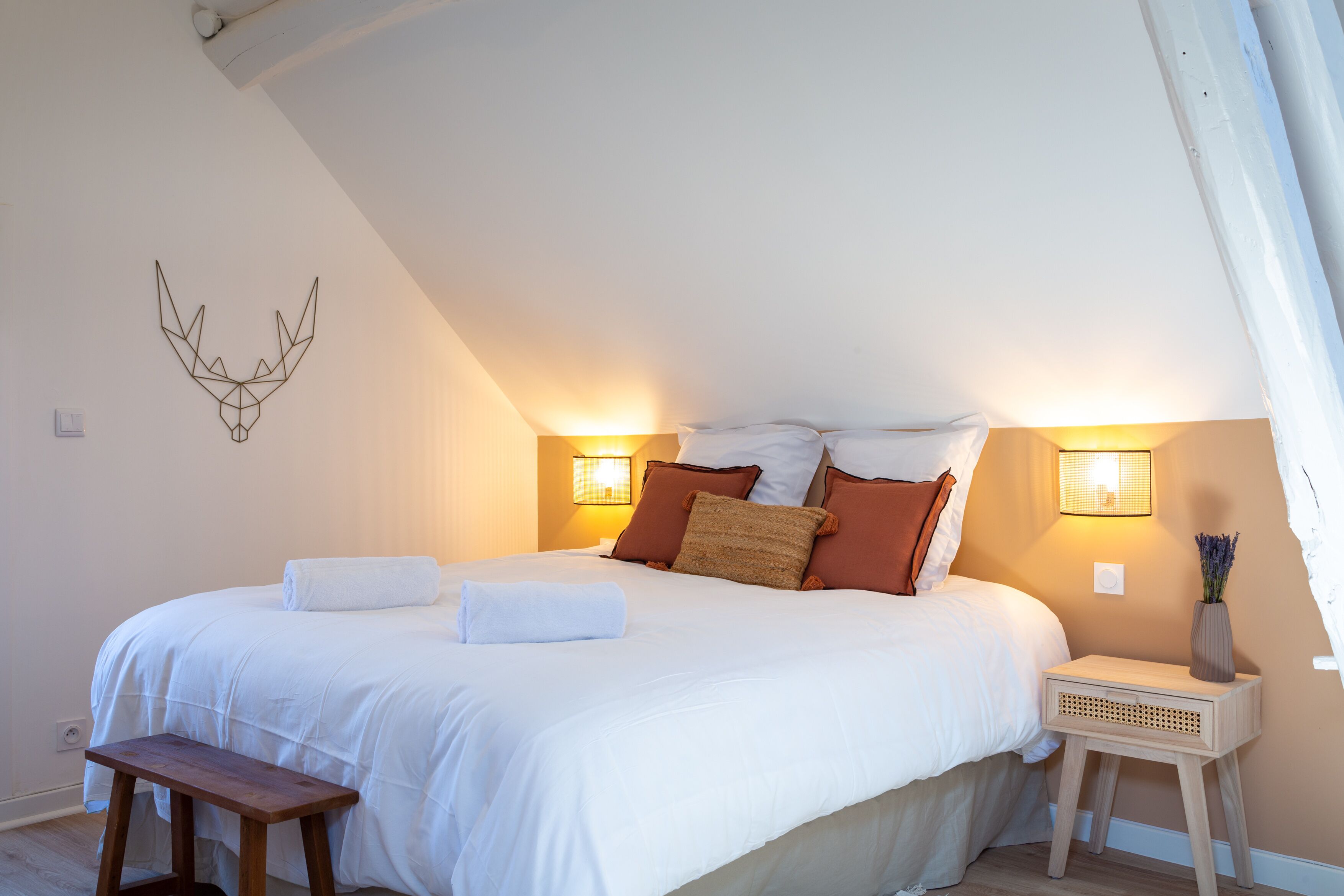 Une chambre avec un grand lit, deux lampes de chevet, un banc en bois et un élément décoratif fixé au mur.