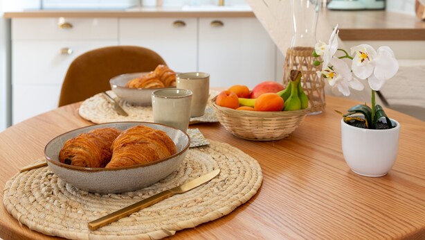 Ein Frühstückstisch mit Croissants, Obst und einer Orchidee im Topf.