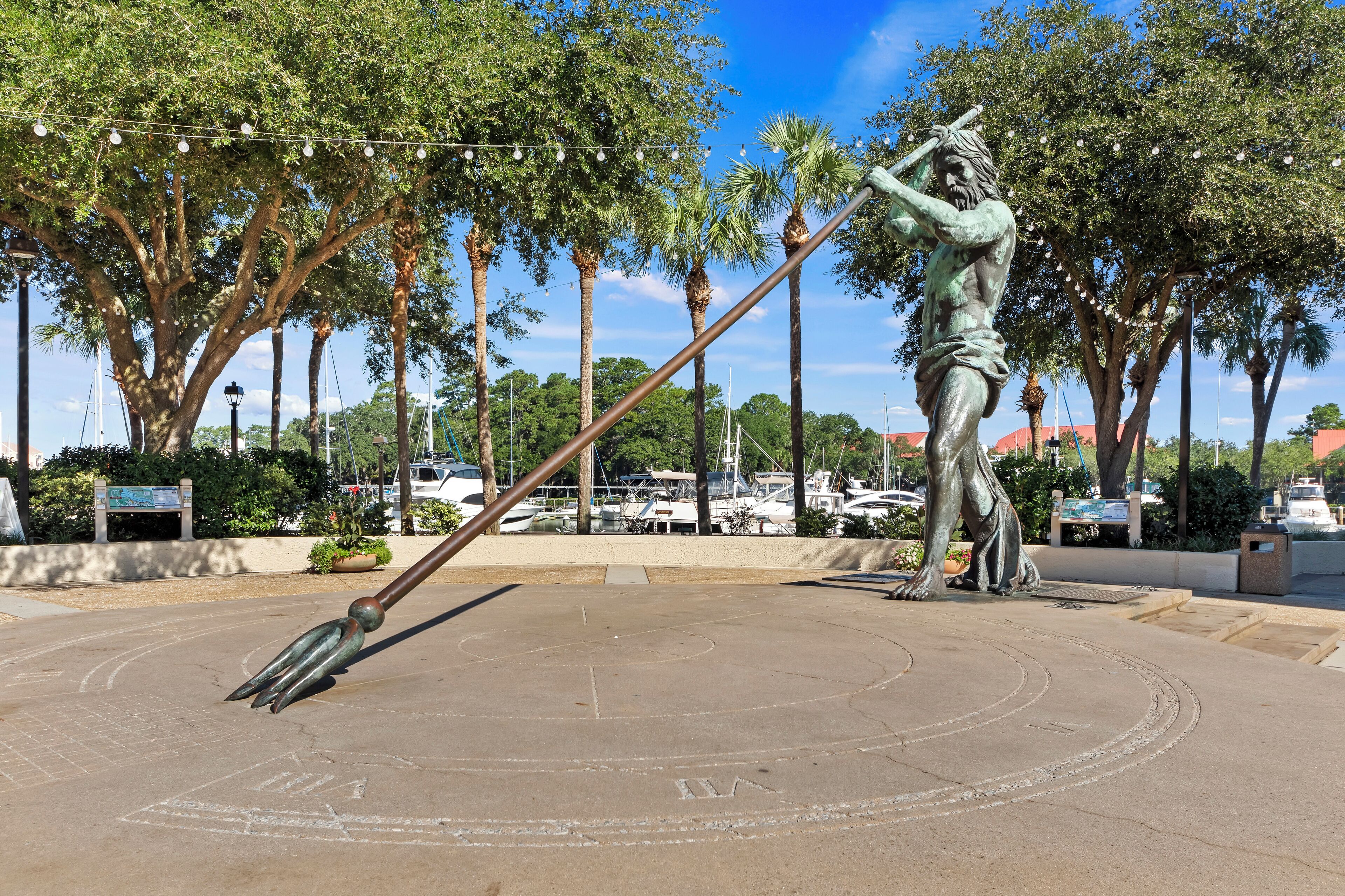 A bronze statue of a figure holding a trident in a public square with palm trees and a clear sky.
