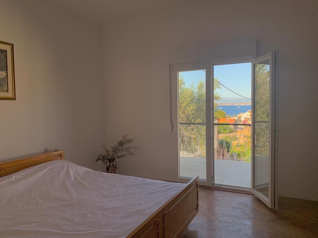 Une chambre à coucher avec un lit, un vase de fleurs et une vue sur l’extérieur, visible à travers une porte vitrée.
