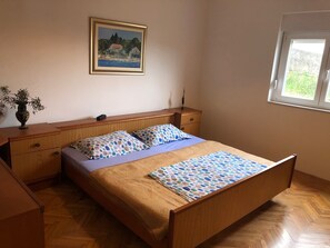 A bedroom with a wooden bed, two pillows, a nightstand, a vase with plants, and a painting on the wall.