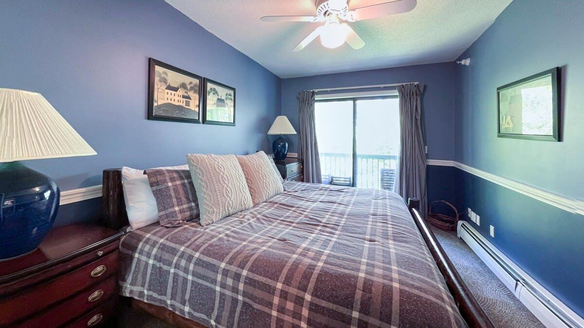 A bedroom with a bed, two bedside lamps, a ceiling fan, and a window with curtains.