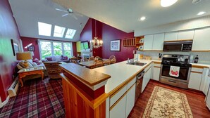 A modern kitchen with white cabinets, a central island, and a dining area with a red carpet. - Cozy 2 BR Ski-in/Ski-out Condo at Okemo (Ludlow)