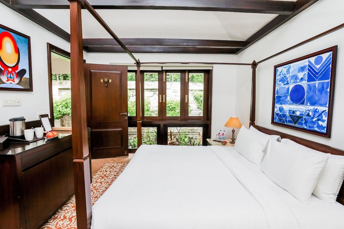 A hotel room with a bed, a desk, a chair, a lamp, and artwork on the walls.
