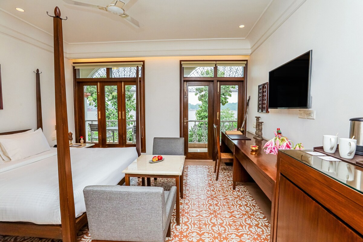 A bedroom with a four-poster bed, a desk, and a chair, a dining table with chairs, and a TV mounted on the wall.