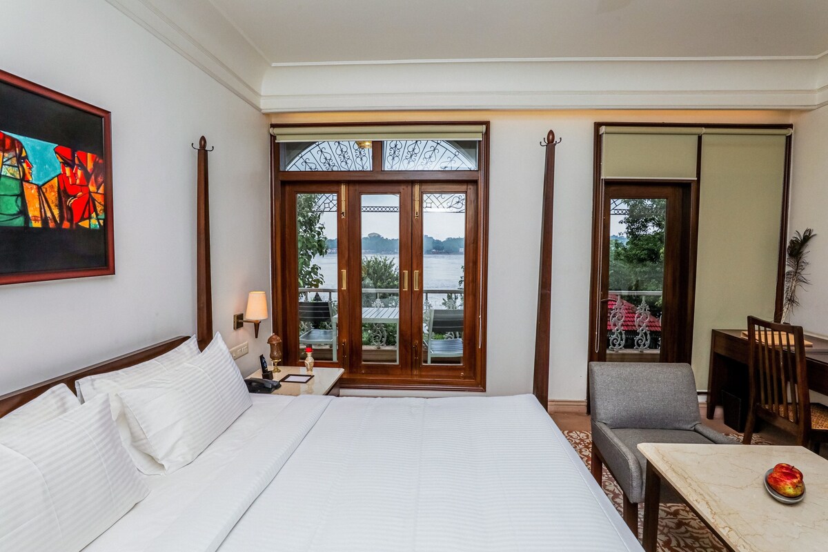 A hotel room with a large bed, a desk, a chair, a table, and a view of a body of water through a glass door.