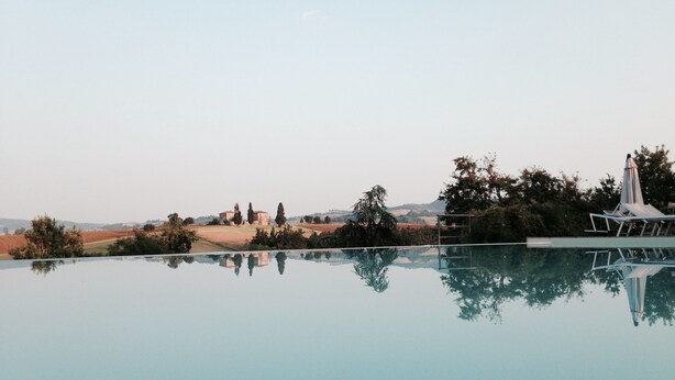 A clear view of an infinity pool with a reflection of the surrounding landscape, including trees and distant buildings.