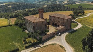 A large, historic building with a courtyard, surrounded by fields and a winding road.