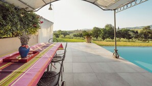 An outdoor patio with a table and chairs, a pool, and a view of the countryside.