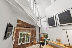 Experience the open, airy feel of this loft-style space with exposed beams, a brick wall, and a wooden staircase.