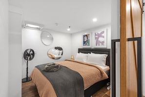 Relax in this serene bedroom with a neatly made bed, round mirror, and framed artworks.