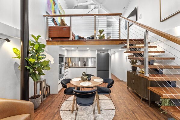 Open-plan living space with a mezzanine level, kitchen, dining area, and wooden staircase.