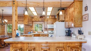 A wooden cabin-style kitchen with a large island, bar stools, and a view of the outdoors.