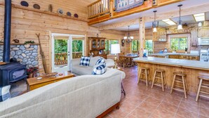 A cozy cabin interior with a stone fireplace, a sofa, a dining area, and a kitchen.