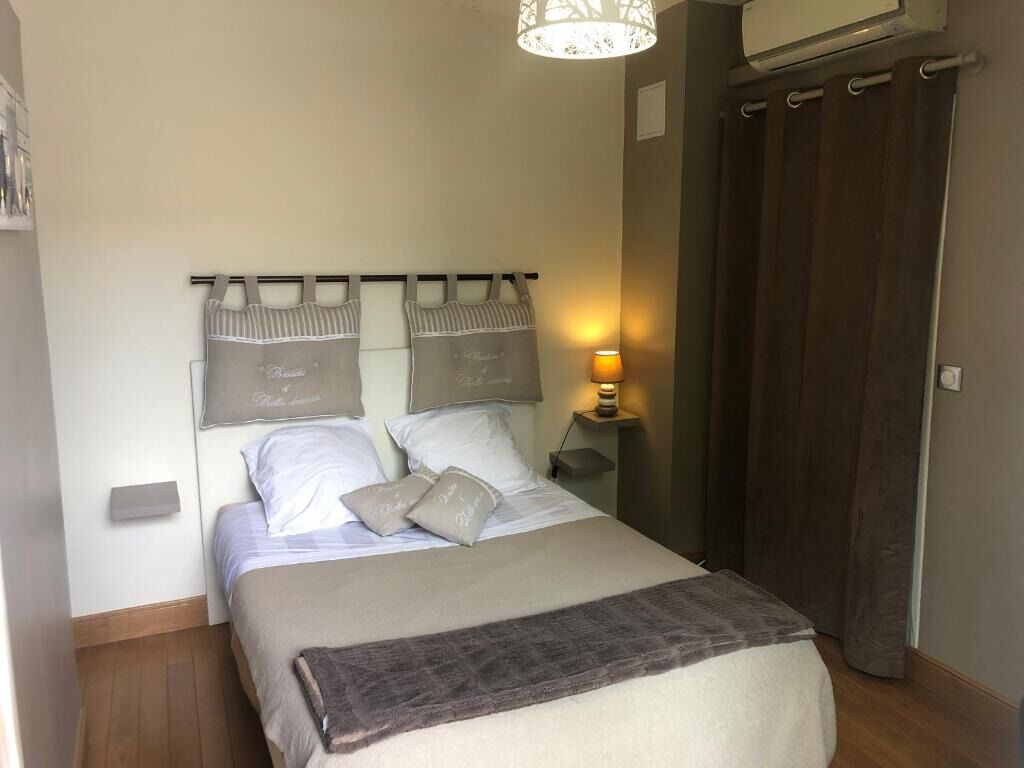 Un lit bien fait, avec une tête de lit, une lampe de chevet et un rideau foncé.