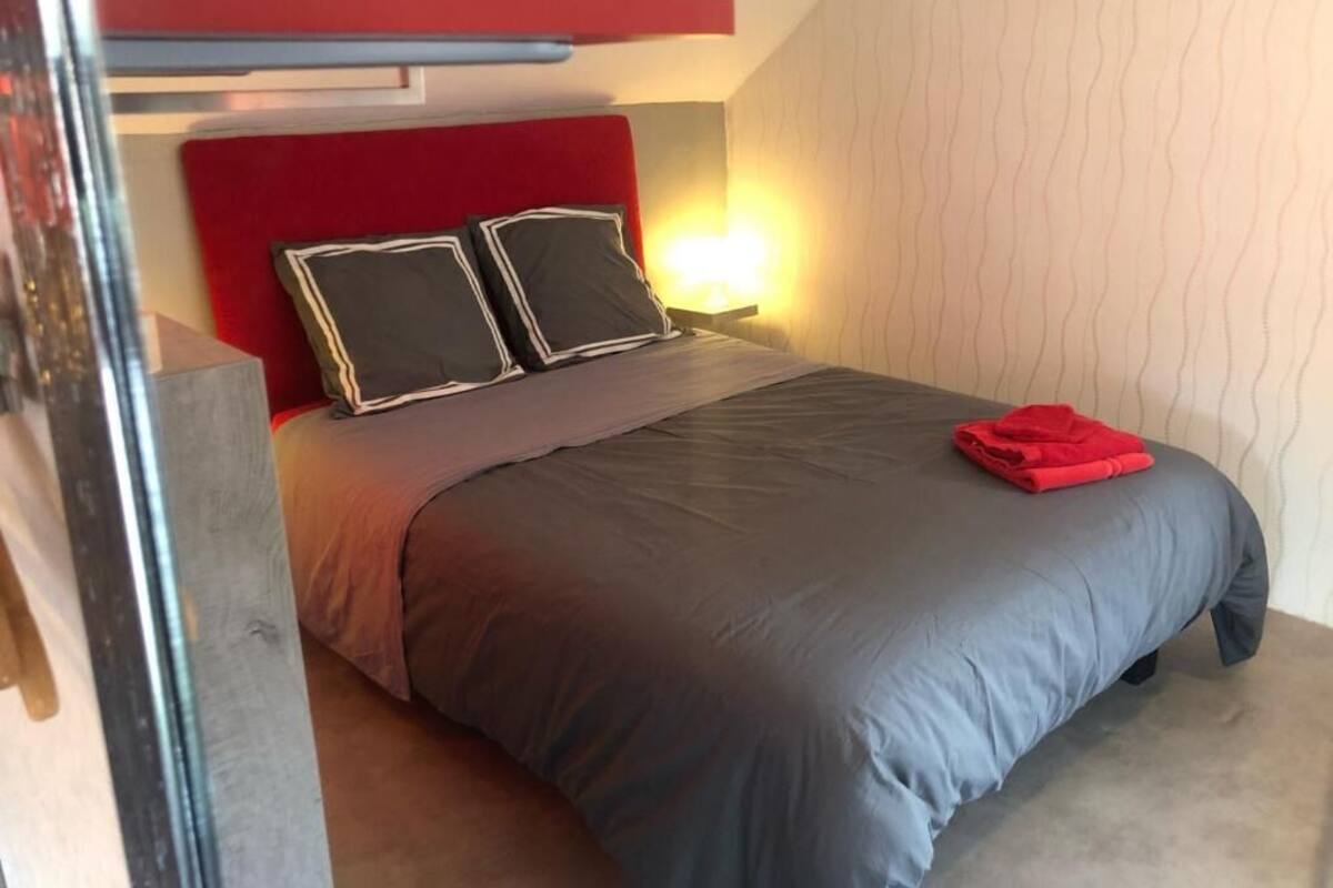 A bedroom with a bed, two pillows, a nightstand, a red headboard, and a wall with a wavy pattern.