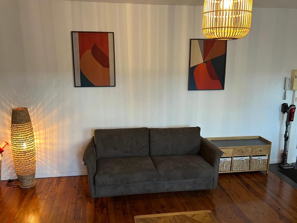 Ein Wohnzimmer mit grauem Sofa, einer stehenden Stehlampe und zwei abstrakten Bildern an der Wand.