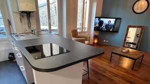 A modern kitchen with a large island, a built-in oven, and a sink. There is a television mounted on the wall and a small table with a chair. - Villa Eugénie, Gîtes & Chambres d'Hôtes  (Melun)