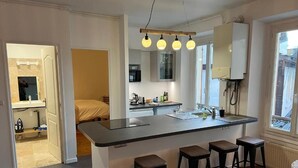 A modern kitchen with a central island, bar stools, and pendant lighting. - Villa Eugénie, Gîtes & Chambres d'Hôtes  (Melun)