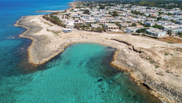 An aerial view of a coastal town with clear turquoise waters, sandy beaches, and a dense cluster of buildings. - 2244 Residence Anna - Appartamento Sarago (Taviano)