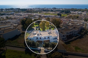An aerial view of a residential area with a highlighted building featuring a central courtyard, surrounded by other buildings, and a coastline in the background. - 2244 Residence Anna - Appartamento Sarago (Taviano)