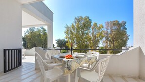 A balcony with a table set for two, white plastic chairs, and a bottle of wine. - 2246 Residence Anna - Appartamento Orata (Taviano)