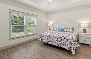 A bedroom with a large bed, two bedside lamps, a nightstand, and a window with blinds.
